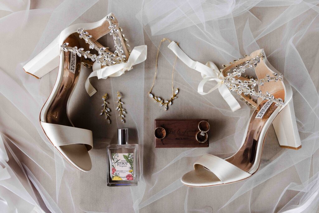 Bridal shoes, perfume, necklace, earrings and wedding rings laying on top of wedding veil