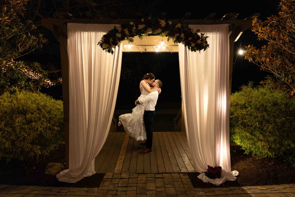 Groom picking up bride outside spinning her around under ceremony site